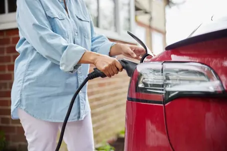 woman charging red car beside brick house